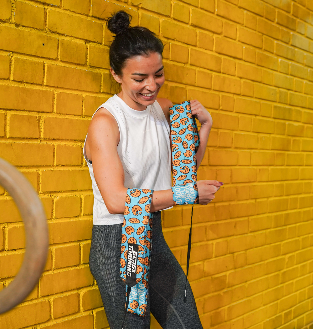 Atleta colocándose una muñequera de tela Cookie junto a una pared amarilla.