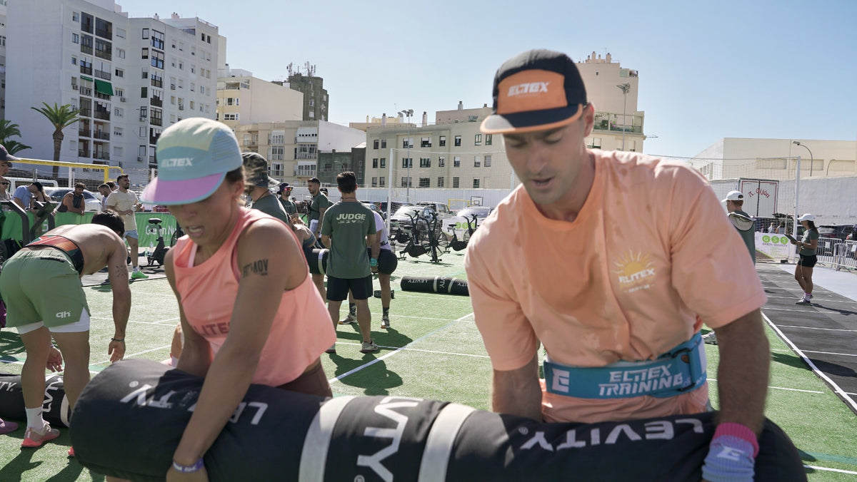 Two athletes wearing AeroFlow caps lifting a training bag together outdoors